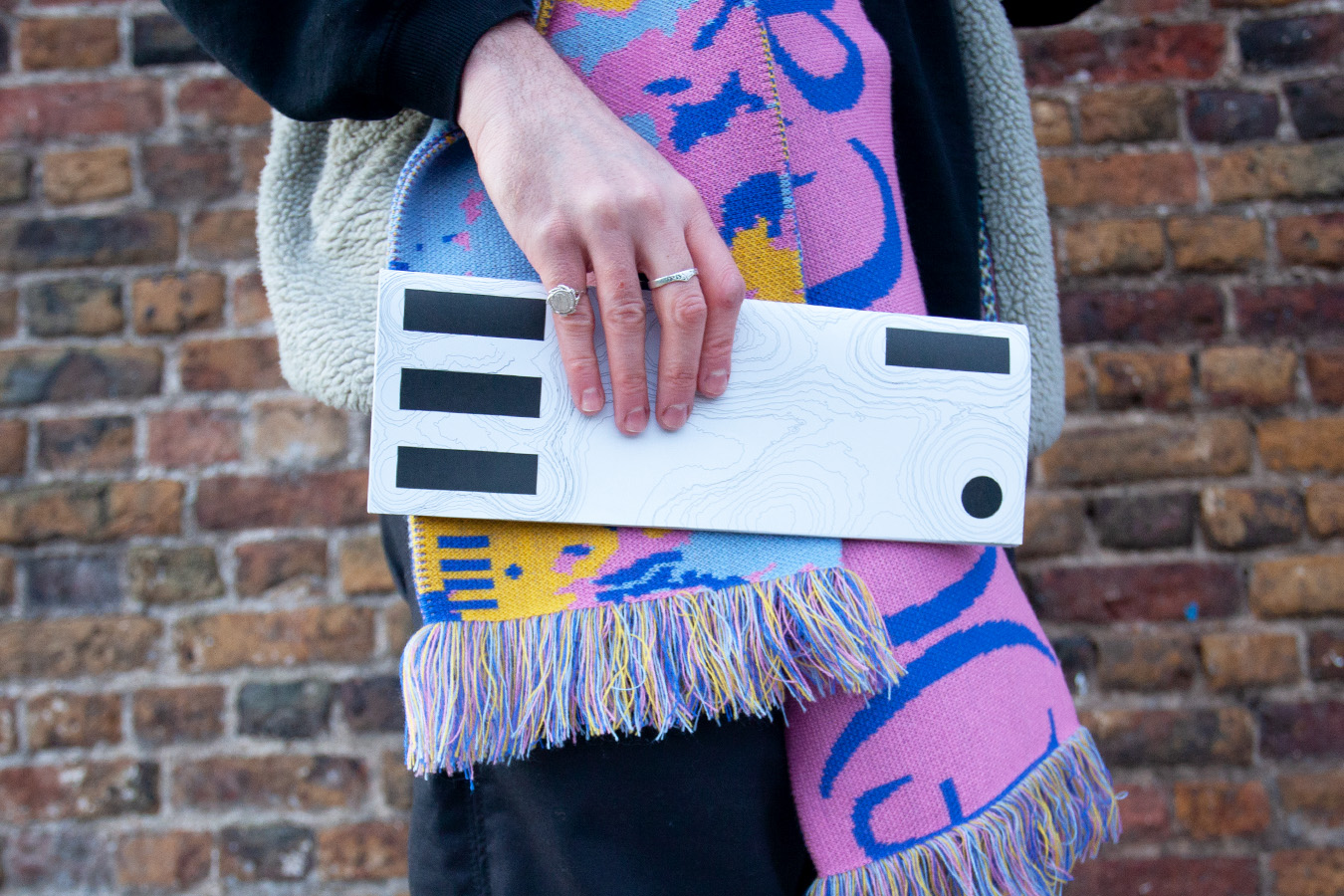 The hero image for Four Eyes or iiii Magazine shows the visual identity for the project through showing a black and white booklet in a persons hand, the person is also wearing a iiii scarf